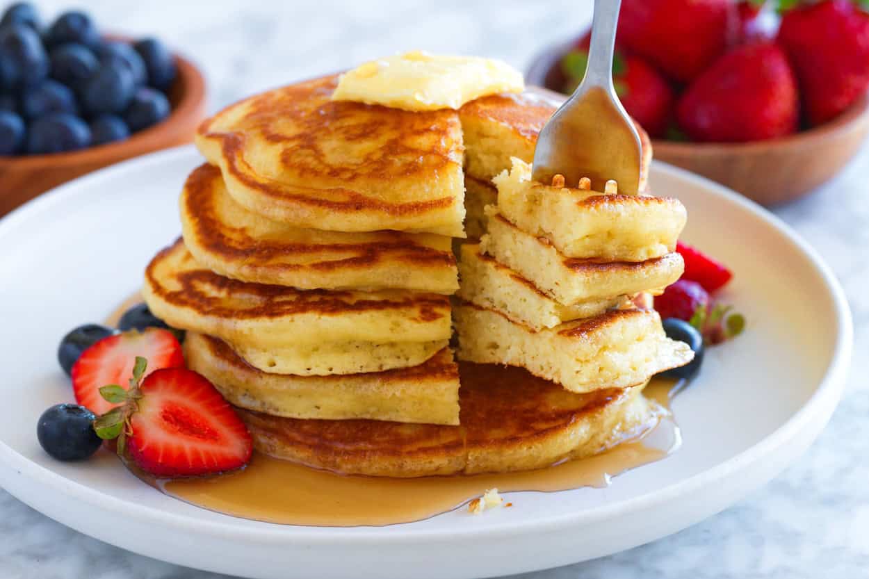 A fork pulling pieces of freshly cooked and fluffy pancakes ready for a bite.