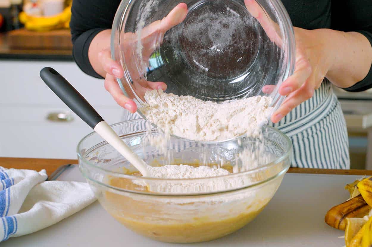 Using a flexible rubber spatula to mix the dry ingredients into the wet ingredients for banana bread