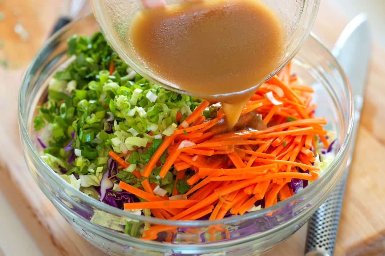 Pouring the dressing over Chinese chicken salad in a large bowl