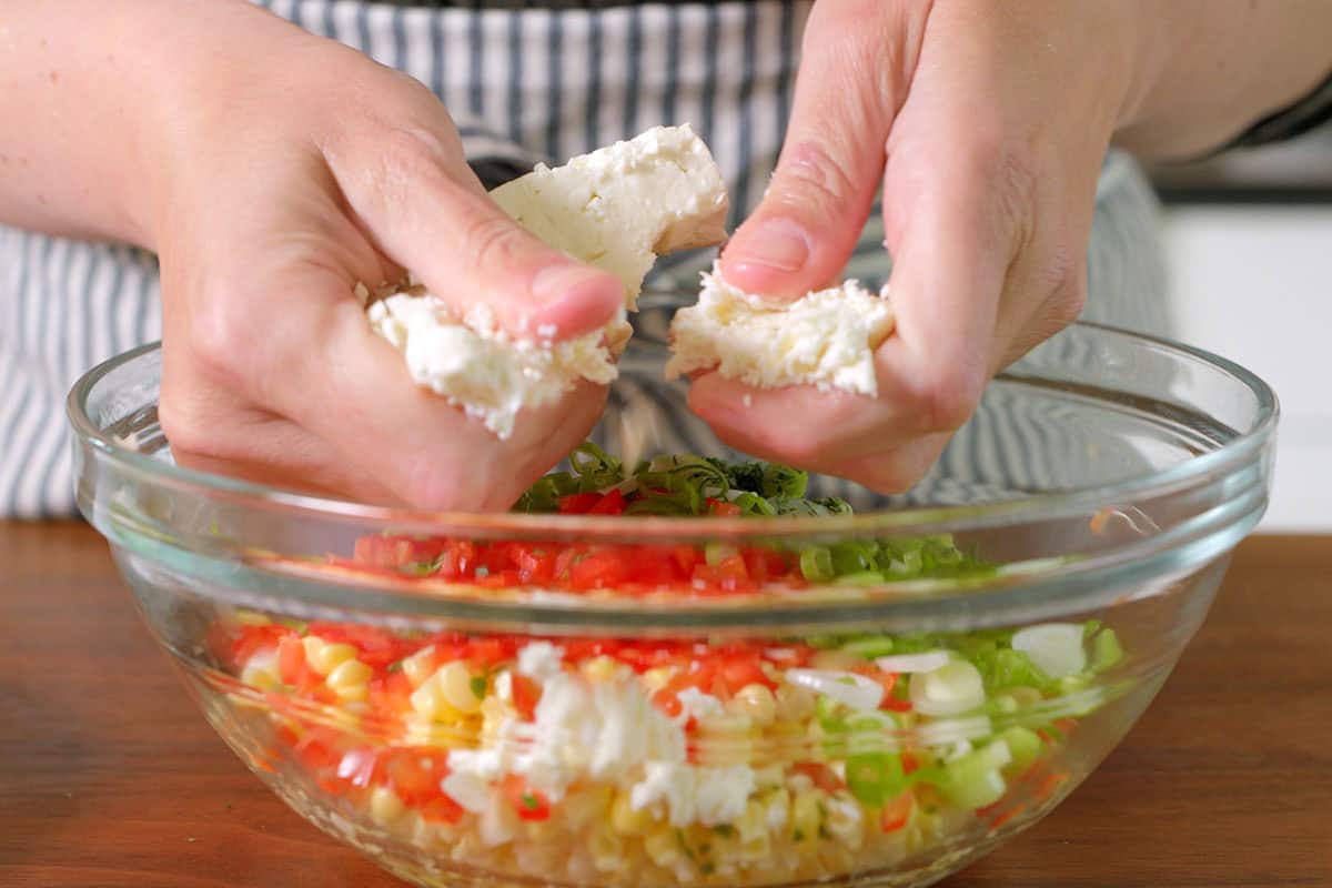 Crumbling feta into the bowl with the other corn salad ingredients