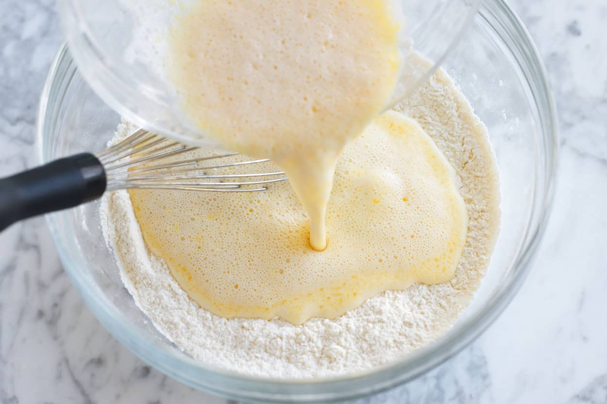 Making pancake batter by pouring wet ingredients (butter, milk, vanilla, and an egg) into flour.