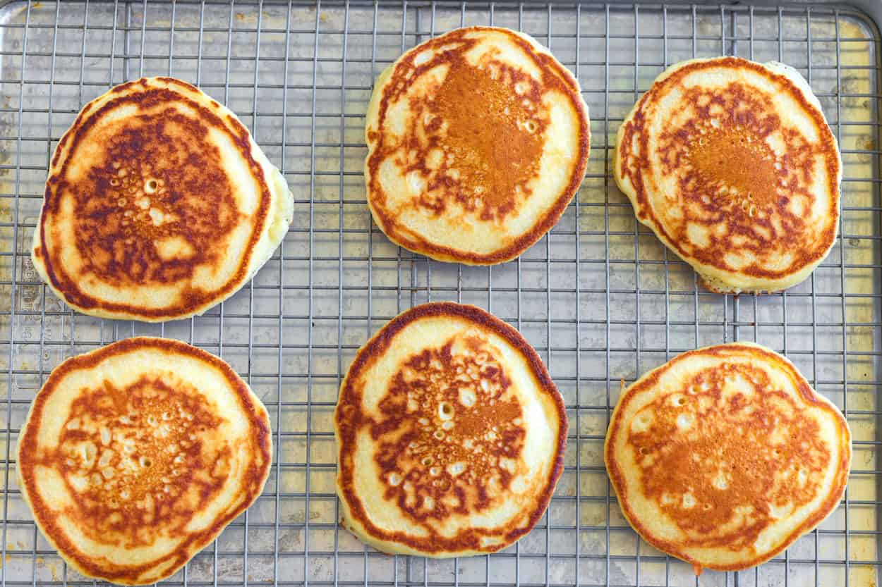 Pancakes lined up on a rack set inside a baking sheet to keep warm in the oven.