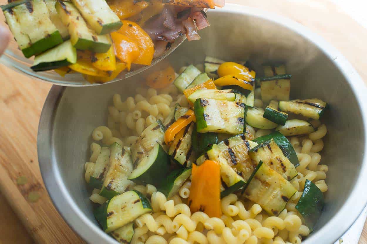 Tossing grilled summer vegetables into a bowl with pasta