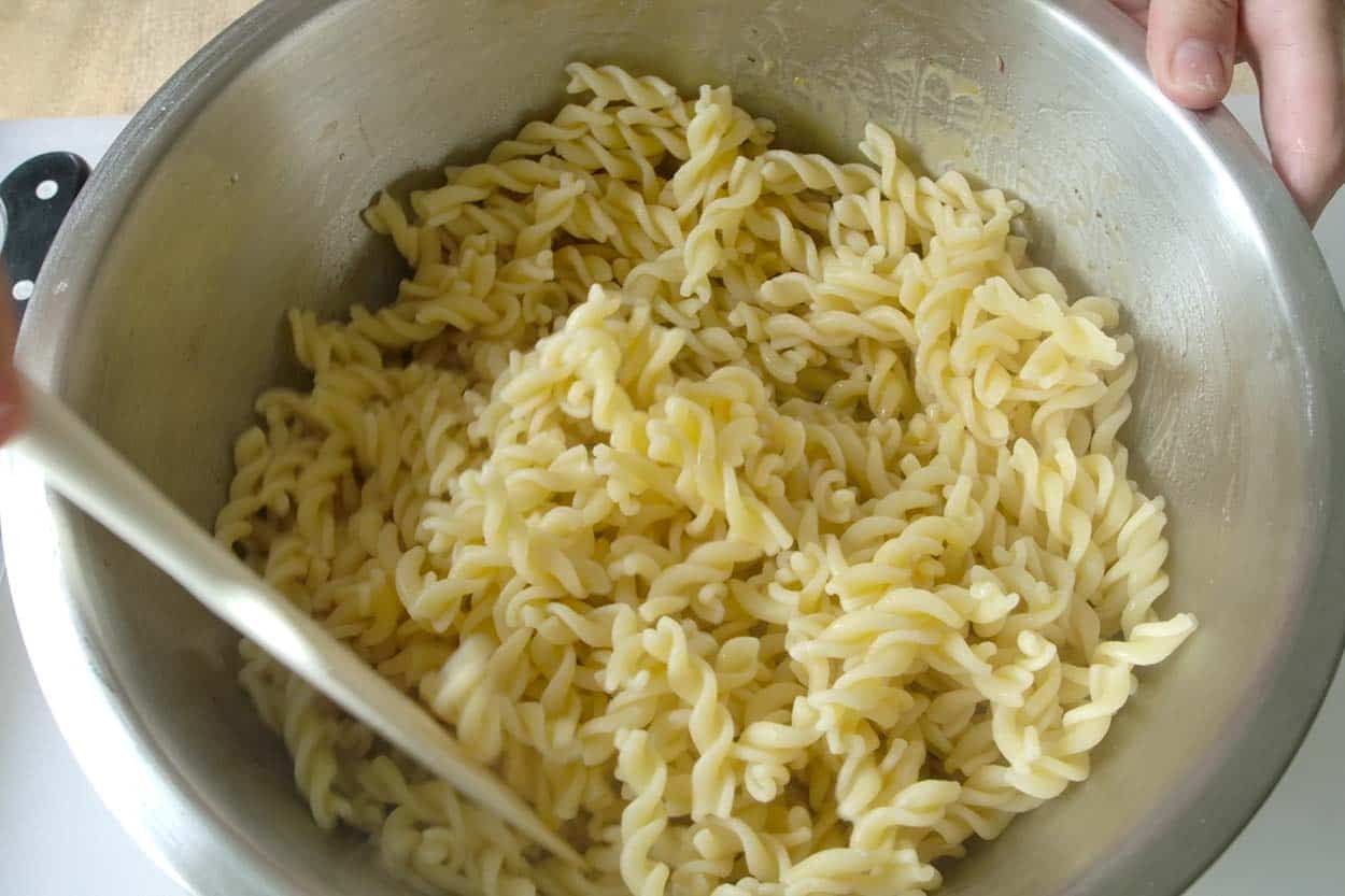 Adding drained and rinsed pasta to the salad dressing in a big bowl