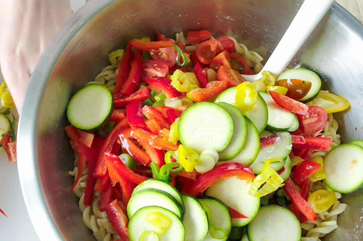Stirring in the remaining pasta salad ingredients (pasta, tomatoes, olives, cheese, red bell pepper)