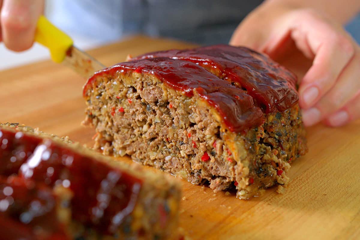 Slicing baked and rested meatloaf with a small serrated knife.