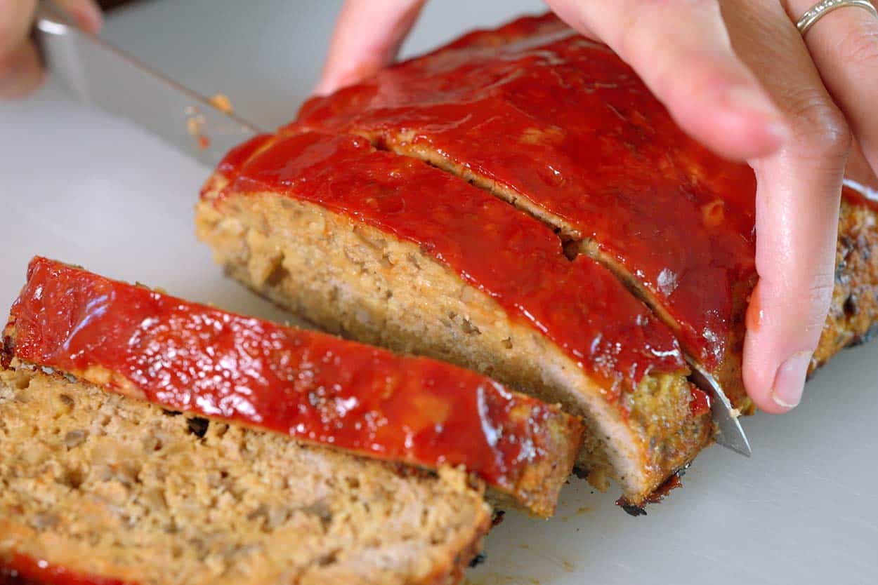 Slicing cooked turkey meatloaf with a serrated knife.